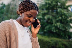 Smiling woman on phone outdoors, representing patient communication with Bracesetters Orthodontics for braces care in Middletown, Monroe, and Newburgh, NY.